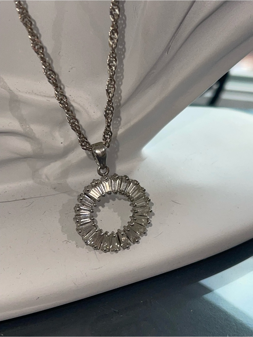 This elegant necklace features a circular pendant accented with a row of radiant